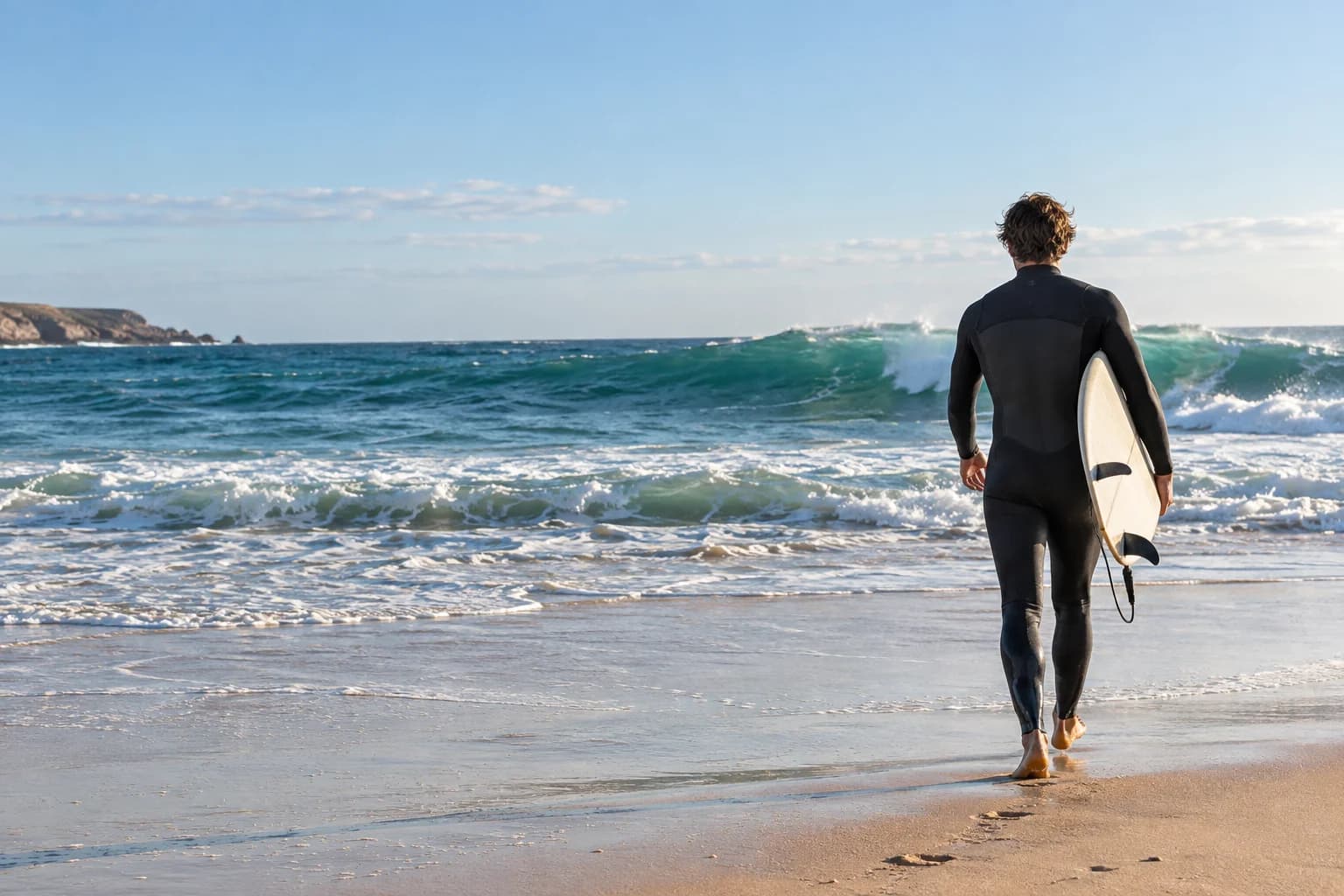 Un surfeur en combinaison face à l'océan